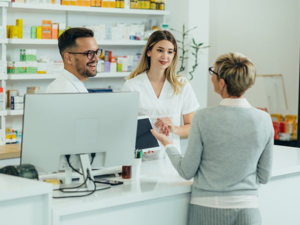 Two pharmacist giving prescription medications to senior female Two pharmacist giving prescription medications to senior female customer in a pharmacy while using digital tablet