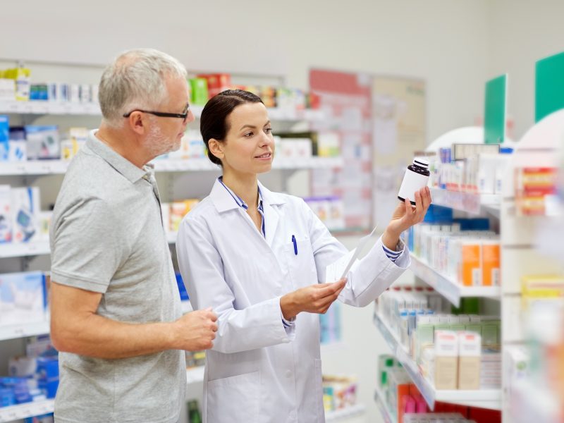 pharmacist and senior man buying drug at pharmacy medicine, pharmaceutics, health care and people concept - happy pharmacist and senior man customer with drug and prescription at drugstore