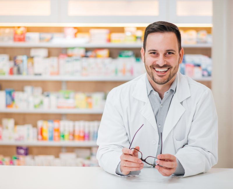 Portrait of a cheerful handsome pharmacist leaning on counter at Portrait of a cheerful handsome pharmacist leaning on counter at drugstore.